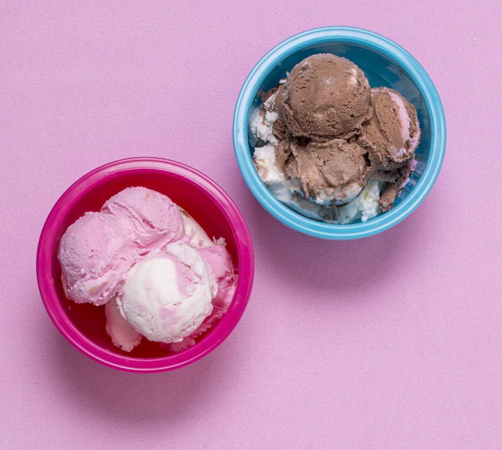 Zwei Eisbecher in Blau und Rosa, gefuellt mit Eiskugeln.